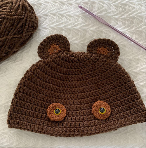teddy bear beanie photo of beanie laid flat on a white background with a crochet hook and yarn 