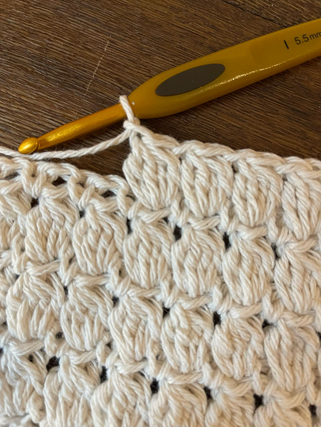 cluster stitch worked in cream coloured yarn on a brown wood background how to crochet the cluster stitch photo 