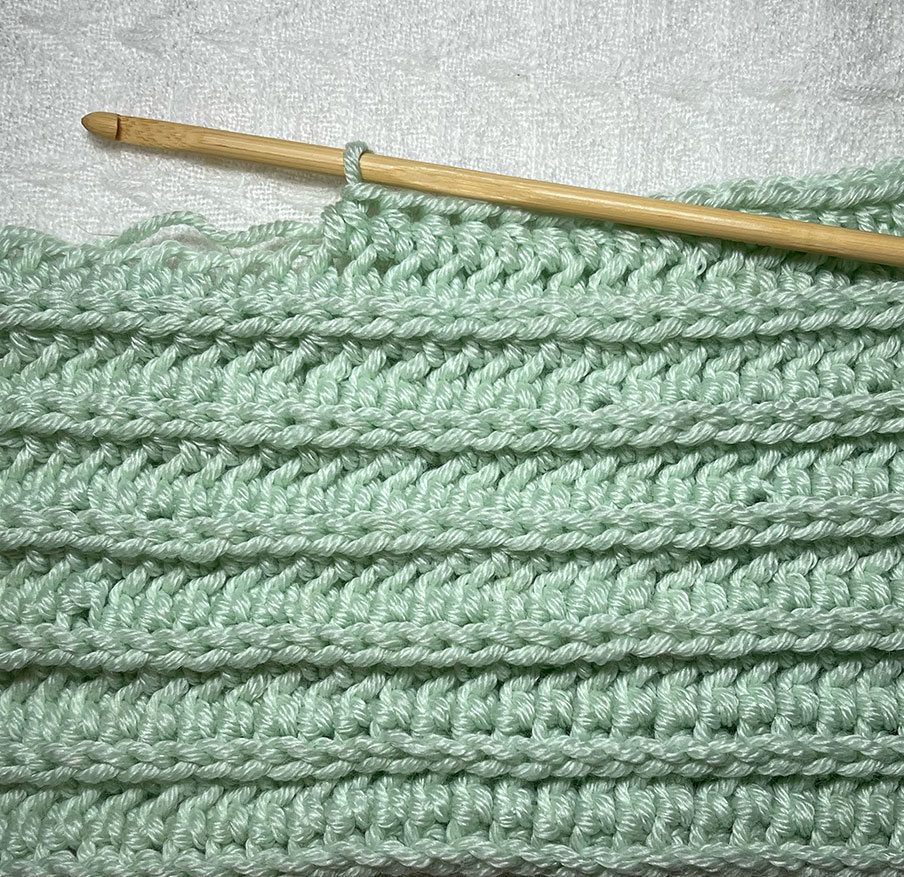 the camel stitch in a green swatch against a white background with a wooden hook 