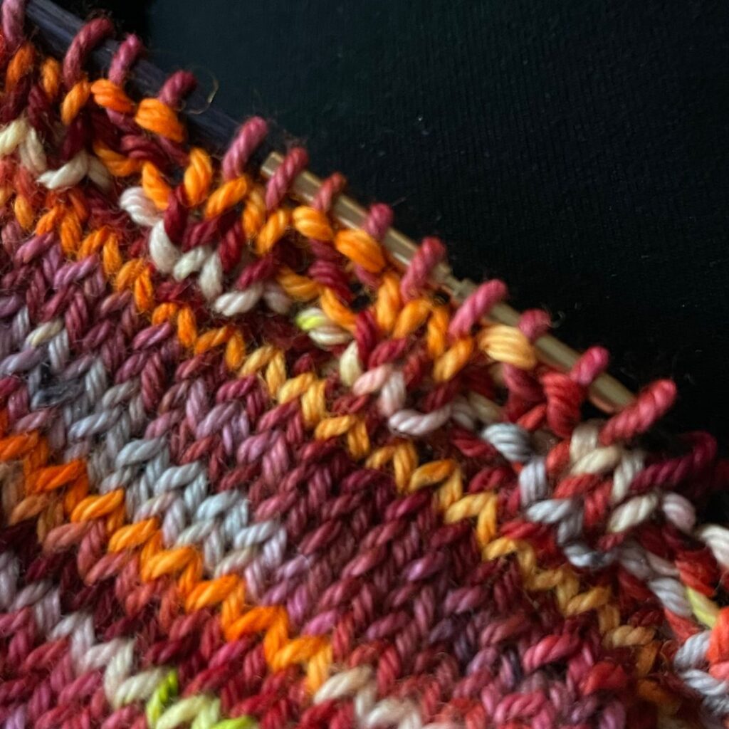 Close up photo of a knitted cowl, incomplete with stockinette stitch and a few rows of ribbing 